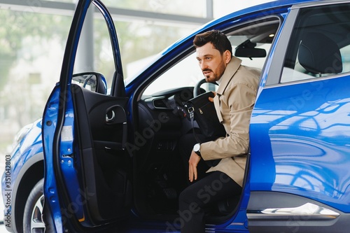 Visiting car dealership. Handsome bearded man is stroking his new car and smiling © Serhii