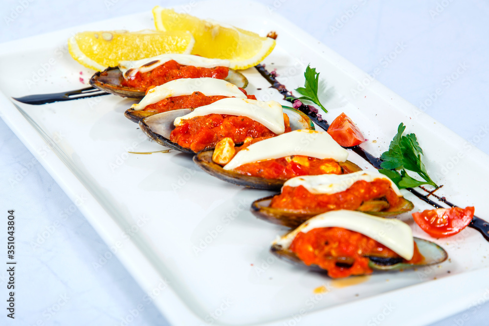 Saganaki mussels: half-baked Mussels, saganaki sauce, feta cheese, lemon. Plate on a white background Saganaki mussels: half-baked Mussels, saganaki sauce, feta cheese, lemon. Plate on a white background