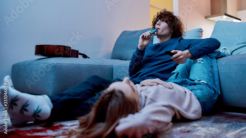 Young creative guy smoking marijuana from a vape pen or vaporizer while relaxing with his girlfriend in the living room