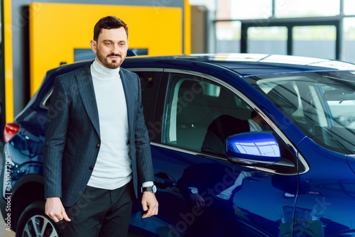 Wallpaper Mural Handsome bearded buyer in casual wear in dealership, guy looks on camera while standing near car with crosed arms Torontodigital.ca