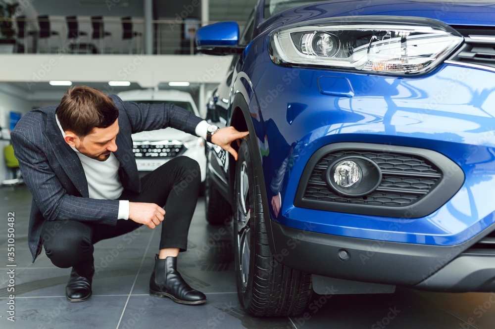 Young handsome man choosing a car in a car showroom Young handsome man choosing a car in a car showroom