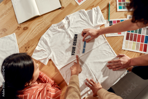 Writing that sells. Creative people trying on stickers with text, while discussing logo and design of T-shirt. Young man and women working together at custom T-shirt, clothing printing company