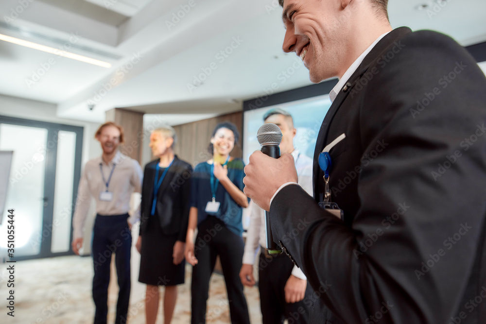 Next Level. Cropped shot of young caucasian male speaker in suit presenting his colleagues while giving a talk at business meeting, economic forum Next Level. Cropped shot of young caucasian male speaker in suit presenting his colleagues while giving a talk at business meeting, economic forum