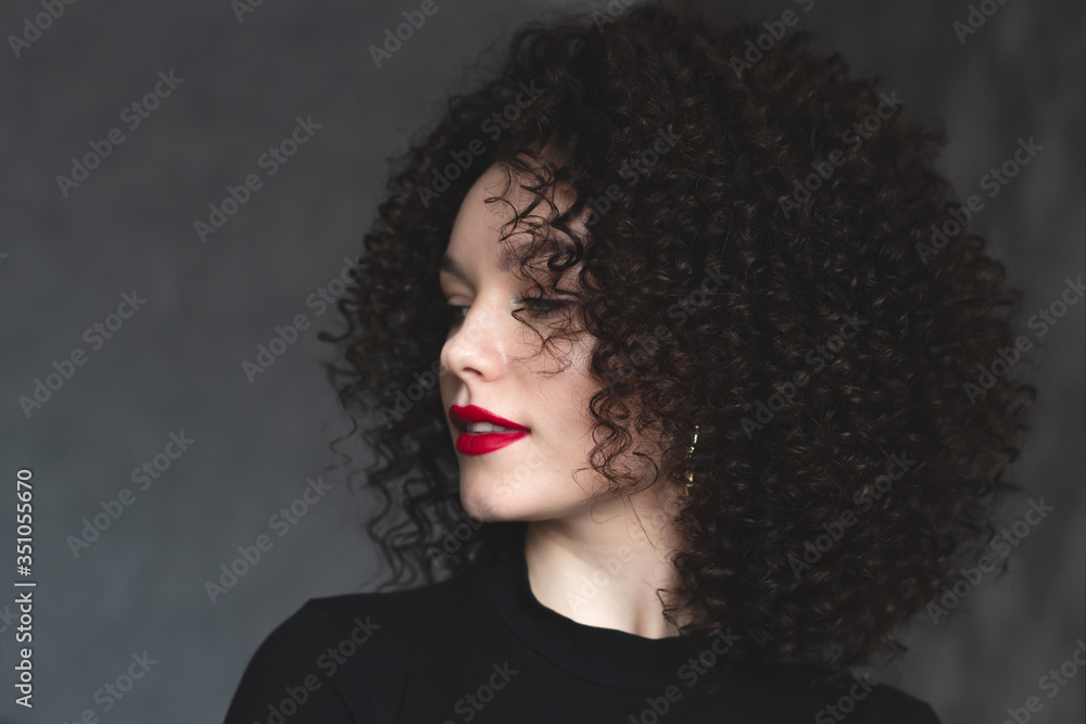 Close-up portrait of a young beautiful girl. Make-up with red lipstick on the lips. Curly hair of the model. Looking off to the side
