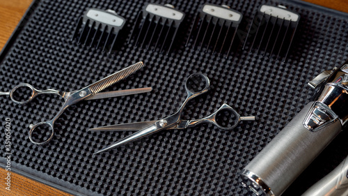 Ready for work. Top view of scissors, electric hair clipper and four different nozzles lying on a rubber mat in the barbershop. Professional barber tool kit