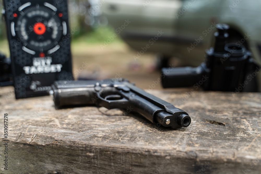 Obraz premium Close up on hand gun replica for airsoft or lasertag laserwar game on the wooden bench or table in nature by other equipment as infrared sensitive target and other weapon