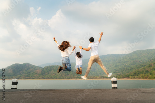 Happy Asian family with father, mother and daughter jumping in road with lake and mountain view in background while vacation together in holiday. Happy family time..