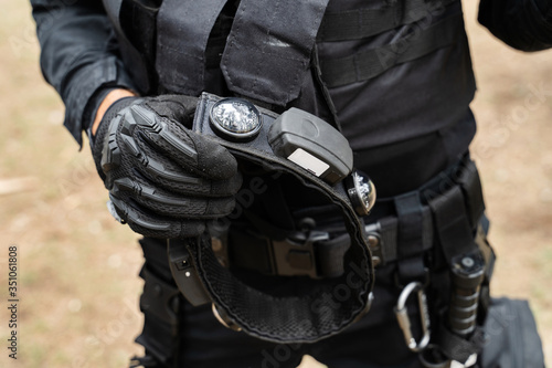 Midsection of unknown man standing in the woods in nature wearing black special forces military or police uniform playing laserwar or lasertag holding smart RGB headband for laser tag