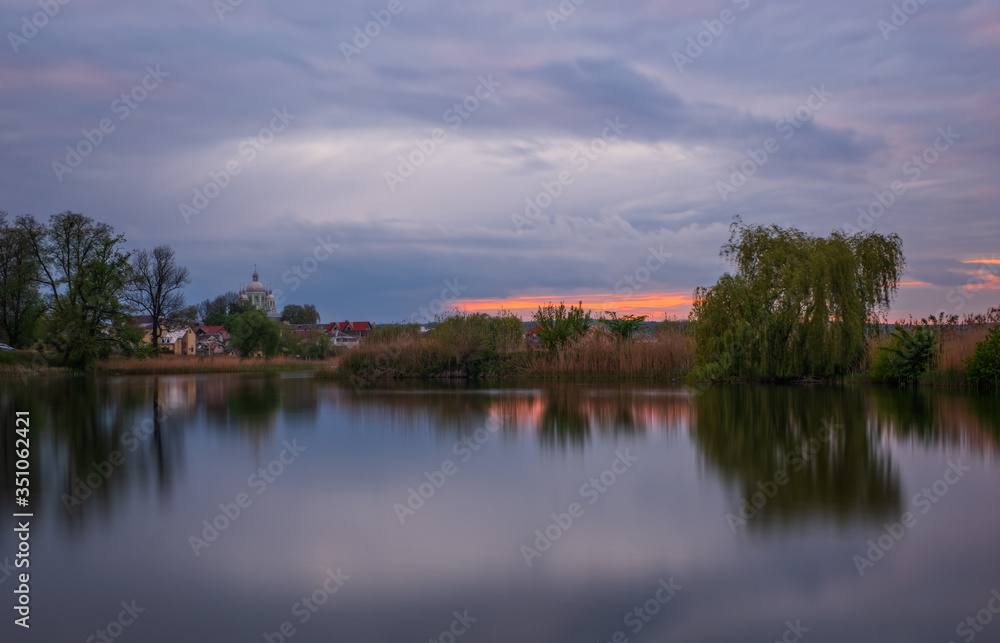 Long exposure sunset view on Ivano-Frankove (Yaniv), Yanivskyi Stav Lake and forest. Roztochia Biosphere Reserve, Lviv district, Ukraine. May 2020