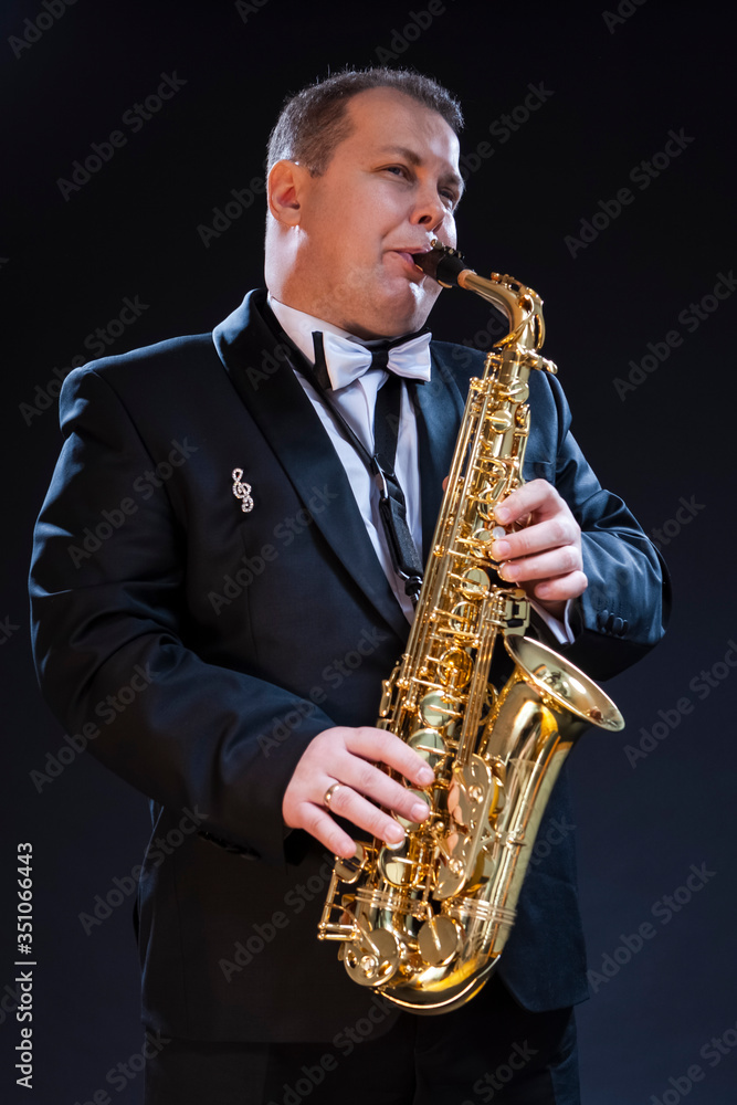 Fototapeta premium Musicians Concepts. Portrait of Mature Expressive Caucasian Saxophonist Against Seamless Black Background.