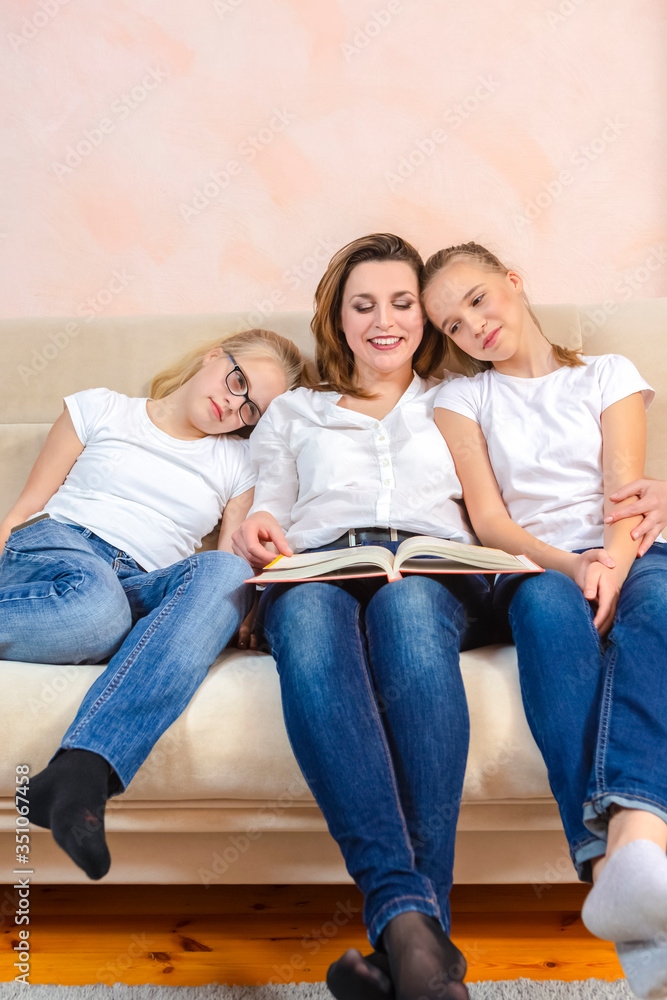 Home Staying Time. Portrait of Young Caucasian Mother Reading a Book Together with Her Twin Daughters While Sitting on Sofa Indoors.