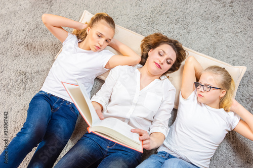 Family Concepts. Portrait of Caucasian Mother Reading a Book Together with Her Female Twins Laying on Floor Indoors.
