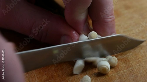 A bunch of fresh green young shoots of garlic are placed on a kitchen wooden cutting board and cut into small circles with a knife. Homemade cooking routine. Vegetable vegan diet. Close-up