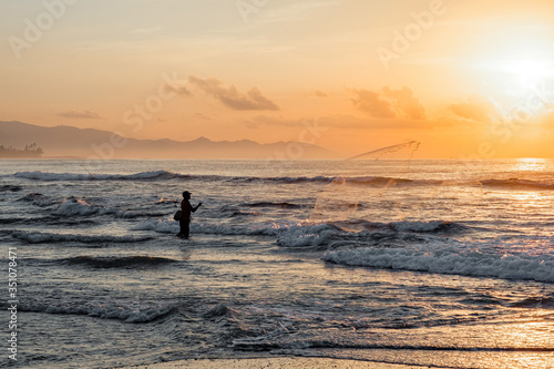 A fisherman throws a net into the sea at dawn. Beautiful sunrise at Pantai Pabean Ketewel Beach on the east coast of Bali.