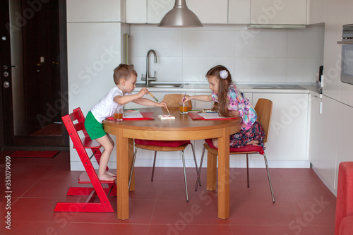 Seven year old girl and three year old boy paint in the kitchen. Modern home interior with white and red colors.  © Юлия Ефимова