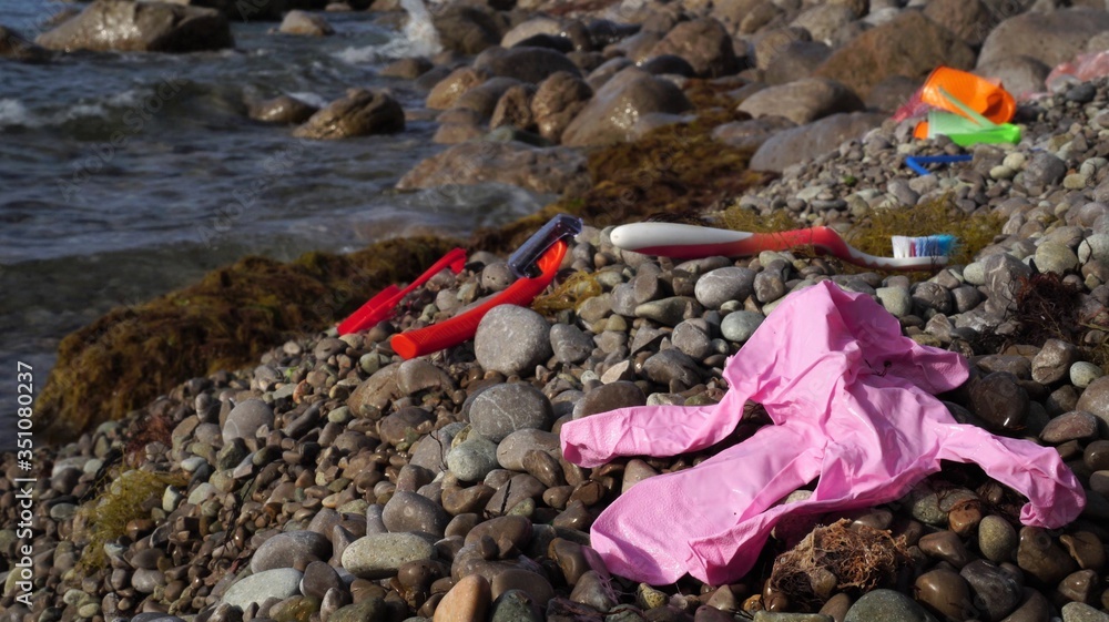 Old used discarded latex glove, toothbrush, disposable razor in a seashore. Garbage in nature