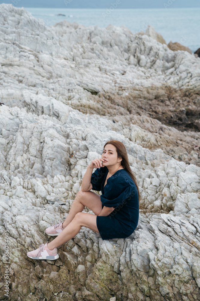 Portrait of young asian woman on stones near sea. Beautiful girl is resting on coast, enjoying outdoor recreation at Kaikoura, New zealand. Portrait of young asian woman on stones near sea. Beautiful girl is resting on coast, enjoying outdoor recreation at Kaikoura, New zealand.