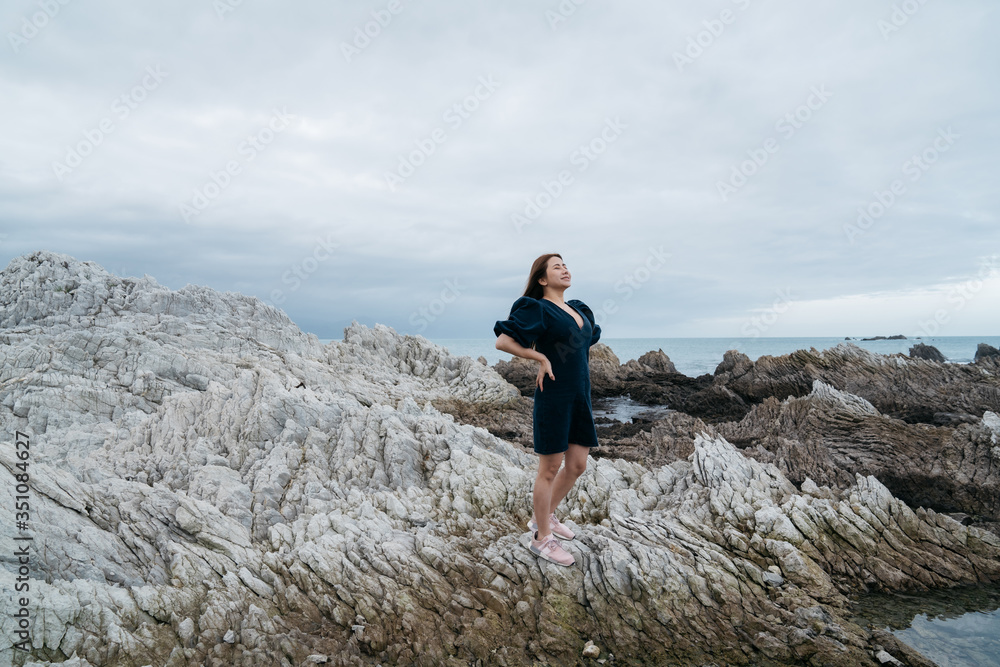 Portrait of young asian woman on stones near sea. Beautiful girl is resting on coast, enjoying outdoor recreation at Kaikoura, New zealand.