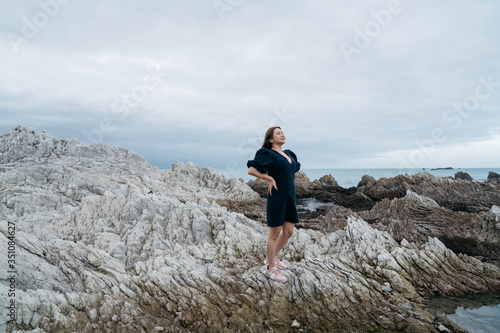 Portrait of young asian woman on stones near sea. Beautiful girl is resting on coast, enjoying outdoor recreation at Kaikoura, New zealand.