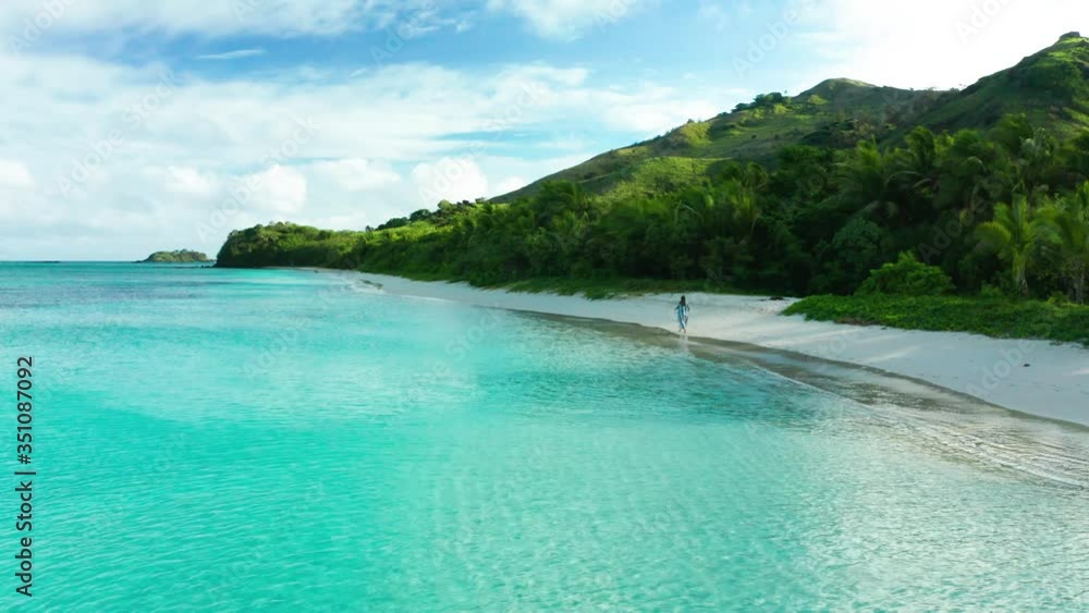 Woman walking alone on isolated beach with lush mountains in background, aerial Woman walking alone on isolated beach with lush mountains in background, aerial