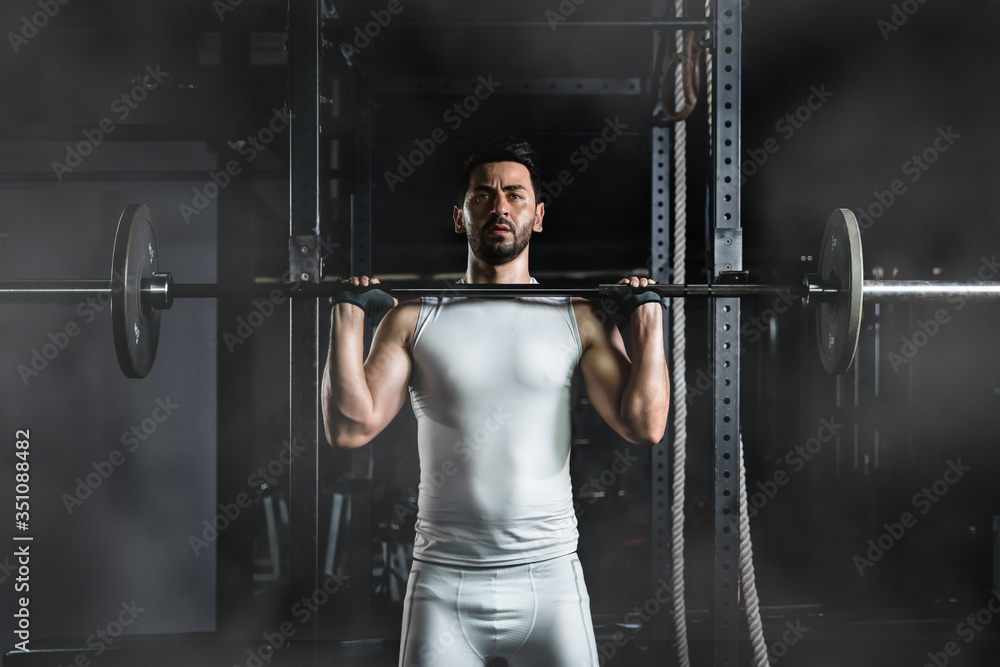 caucasian athletic strong man having workout and bodybuilding with barbells weightlifting front squat style in gym and fitness center in dark tone, selective focused caucasian athletic strong man having workout and bodybuilding with barbells weightlifting front squat style in gym and fitness center in dark tone, selective focused