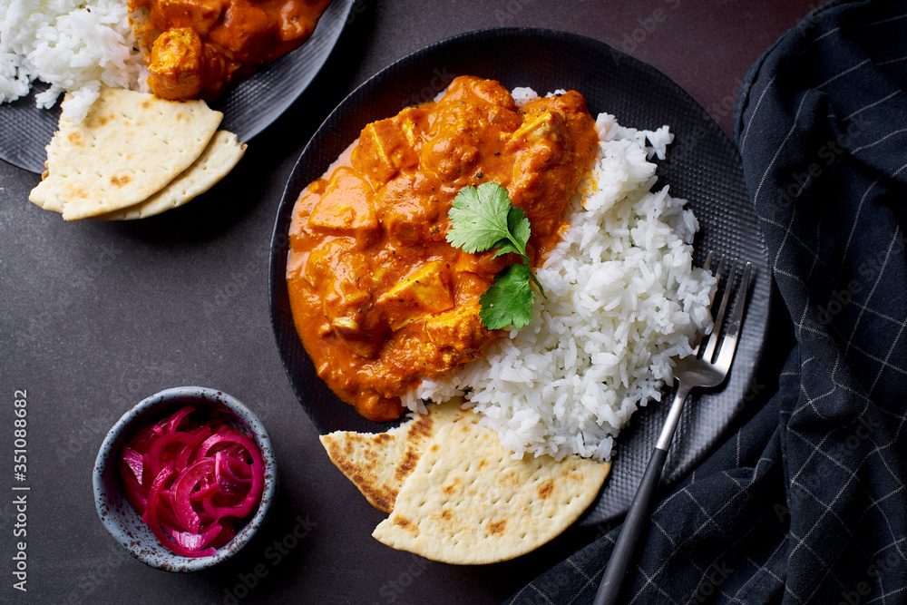 Paneer tikka masala with basmati rice. Indian cuisine, vegetarian dish made of soft cheese cubes cooked in spicy tomato sauce with cream. Top view, dark background. Paneer tikka masala with basmati rice. Indian cuisine, vegetarian dish made of soft cheese cubes cooked in spicy tomato sauce with cream. Top view, dark background.