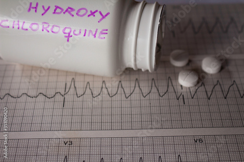 Adverse effects on the heart by hydroxychloroquine or chloroquine. Pills on an electrocardiogram with cardiac arrhythmias. White container with 