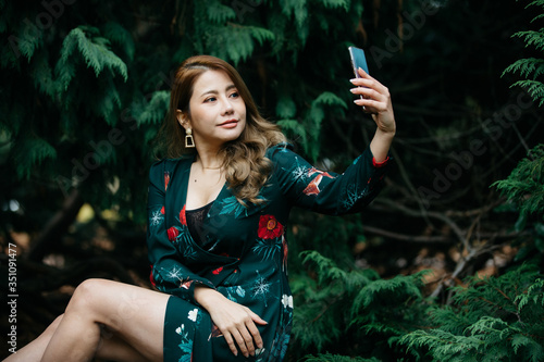 Beautiful asian woman in green dress using cellphone, mibile phone or smartphone pose in the park with green leaves. photo