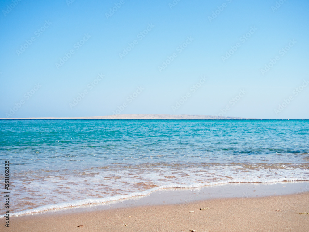 Red Sea photographed from beach, long view. Sea foam on brown sand. Blue sky is clear. Egypt in february, nature background. Selective soft focus. Blurred background