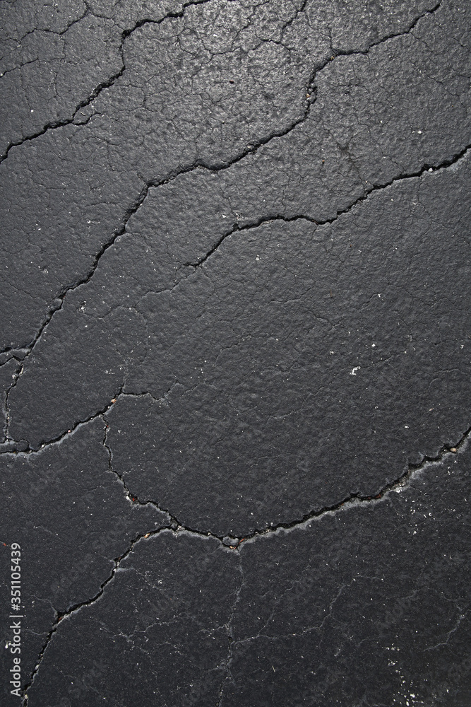 Obraz premium cracked black asphalt surface, texture, pattern, background. Vertical photo. Flat lay.