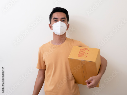 Happy delivery service employee in medical face mask carry cardboard box in hand