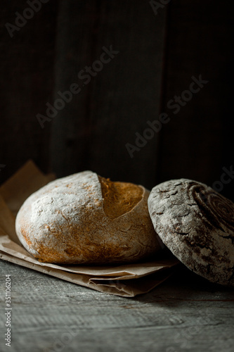 Healthy rye whole grain round bread on brown craft paper on black wooden table. Home baked