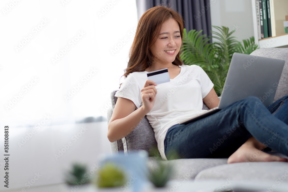 Beautiful young woman sitting on the sofa at home. She is holding a credit card and uses a laptop computer to shop online at home. Beautiful young woman sitting on the sofa at home. She is holding a credit card and uses a laptop computer to shop online at home.