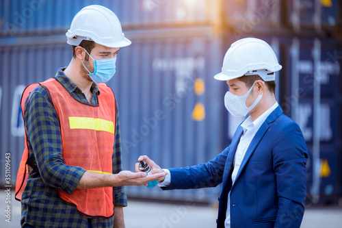 Engineer dock worker apply alcohol gel to clean hand for protect covid-19 virus spread to worker and engineer in dock container ,wearing face mask to safe from virus and pollution.