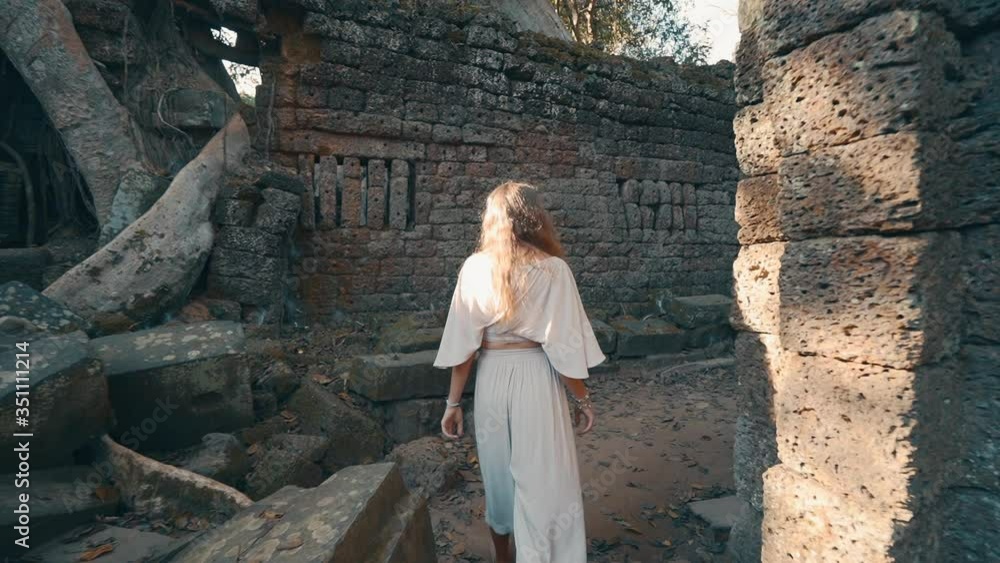 A young woman walking amongst the toppled stone ruins of Ta Prohm Temple, Cambodia, slow motion A young woman walking amongst the toppled stone ruins of Ta Prohm Temple, Cambodia, slow motion