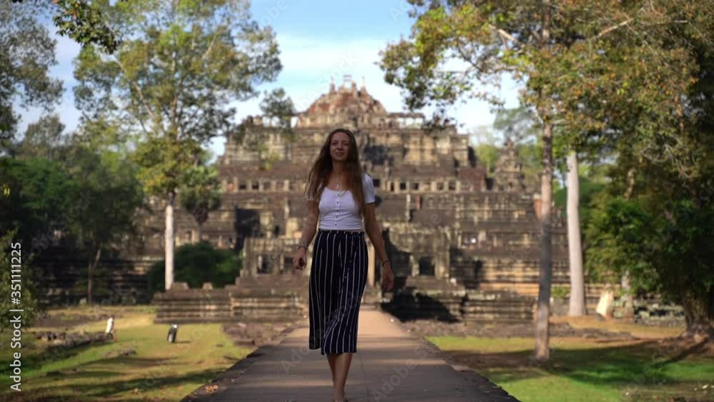 A young woman walks down a path in front of Hindu Temple Baphuon, Angkor Cambodia, slow motion A young woman walks down a path in front of Hindu Temple Baphuon, Angkor Cambodia, slow motion