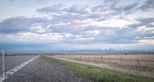 Road leading to horizon with mountains in backdrop, shot during sunset in Southern Alberta, Canada