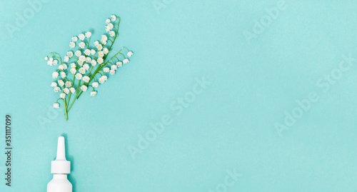 Allergy concept. Antihistamine drug, nose spray against allergies to pollen of flowering plants, spattering spring blossom of lilies of the valley. Top view on blue background and copy space. photo