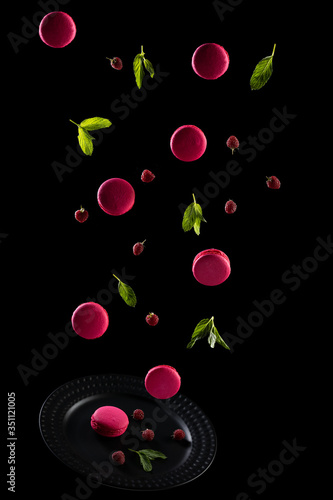 Pink raspberry macaroons. French cookies macarons, levitates with fresh berries and mint leaves on a black background