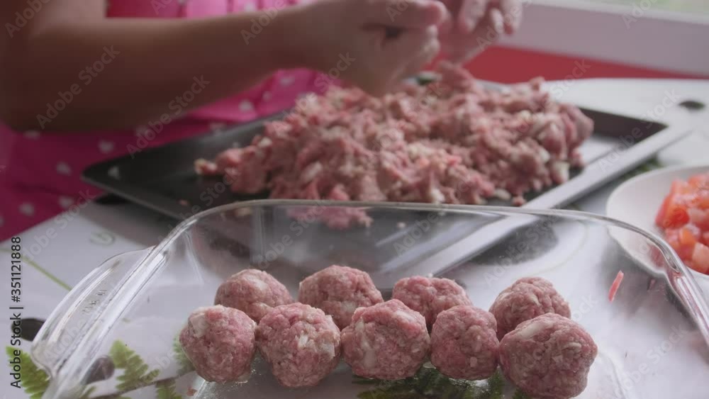 Making meatballs with the hands from fresh seasoned ground meat and putting them in a glass container. Close up shot. 