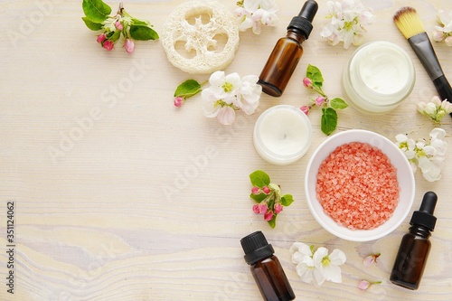 Face and body skin care products, beauty, spa composition with bath salt, essential oils, creme, cosmetic brush, flat lay with spring flowers.