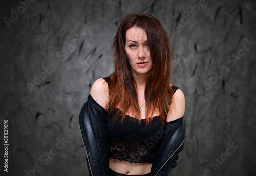 Studio portrait of a caucasian young brunette woman with minimal makeup. A pretty model is standing on a gray background in a black jacket. © Вячеслав Чичаев