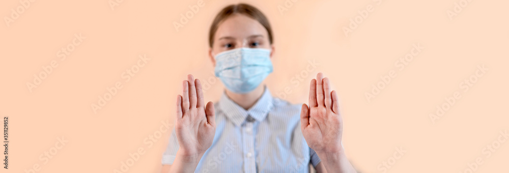 Fototapeta teenage girl on beige background, focus on hands, stop gesture hand, in medical mask, carefully virus and flu virus and disease, stay home, stop pandemic of coronovirus covid 19