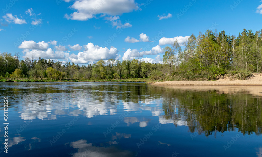 spring landscape with a river, in the waters of which clouds are reflected, the river banks are covered with trees, the first spring greenery in nature