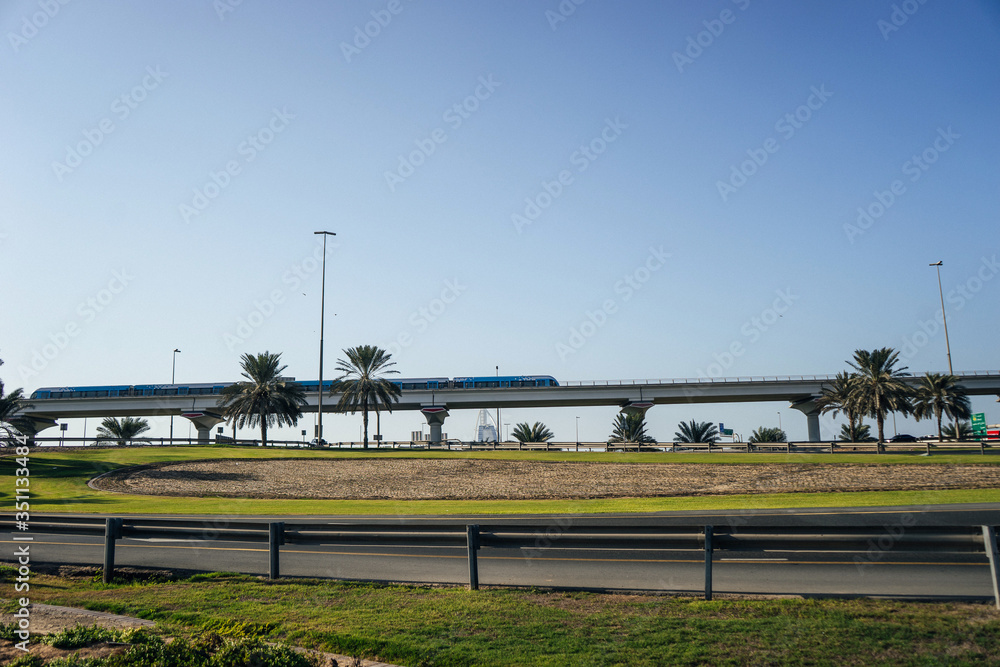 A metro train rides over a bridge over a city where palm trees grow | UNITED ARAB EMIRATES, DUBAI - 17 OCTOBER 2017. A metro train rides over a bridge over a city where palm trees grow | UNITED ARAB EMIRATES, DUBAI - 17 OCTOBER 2017.
