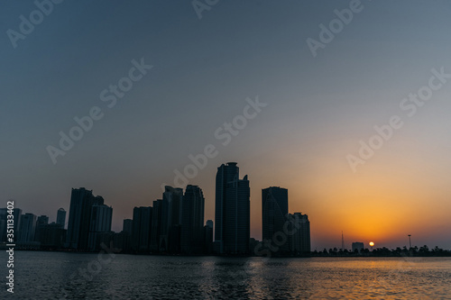 Evening sunset on the seashore and city silhouettes of tall houses on the other Bank | UNITED ARAB EMIRATES, SHARJAH - 17 OCTOBER 2017.