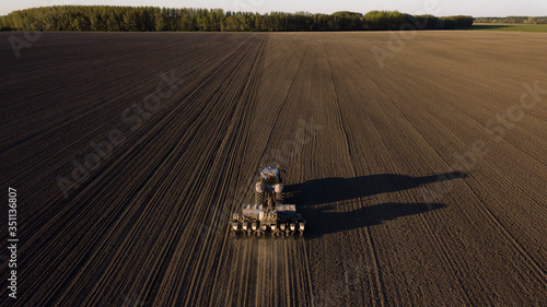 Tractor plows, cultivates the soil at sunset. Drone shot from above.