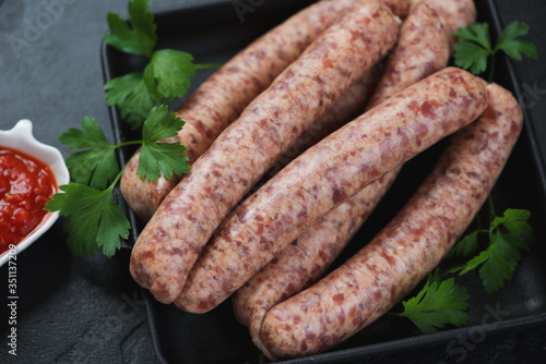 Close-up of raw pork and poultry sausages with fresh parsley in a cast-iron tray, selective focus, studio shot