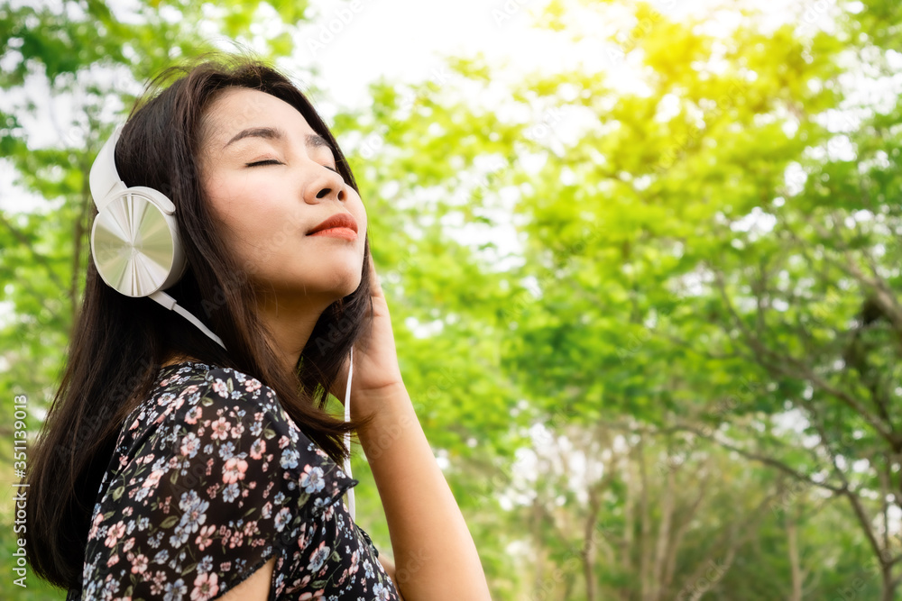 Relaxed Asian woman wearing headphone enjoying the music outdoors while walking in a green park