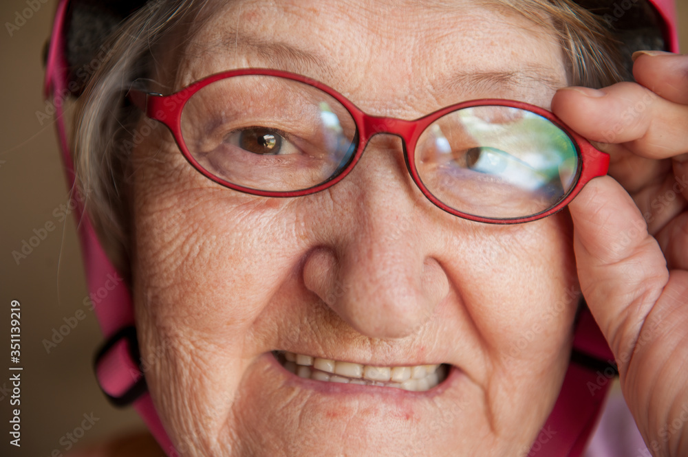 Portrait of elderly woman in pink T-shirt and sports bike helmet and glasses. Pensioner maintains health and cycling, makeup bag Portrait of elderly woman in pink T-shirt and sports bike helmet and glasses. Pensioner maintains health and cycling, makeup bag